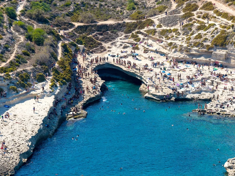 St Peter’s Pool at Delimara from above: a limestone inlet with swimmers on the rock ledges