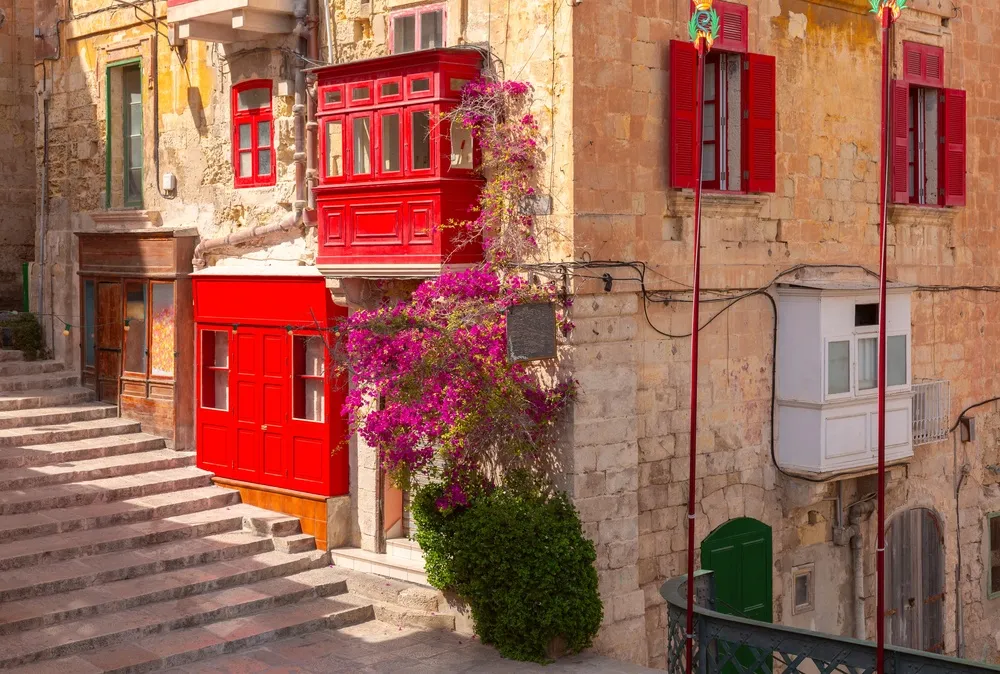 A stepped street in Valletta with red enclosed wooden balconies and bougainvillea